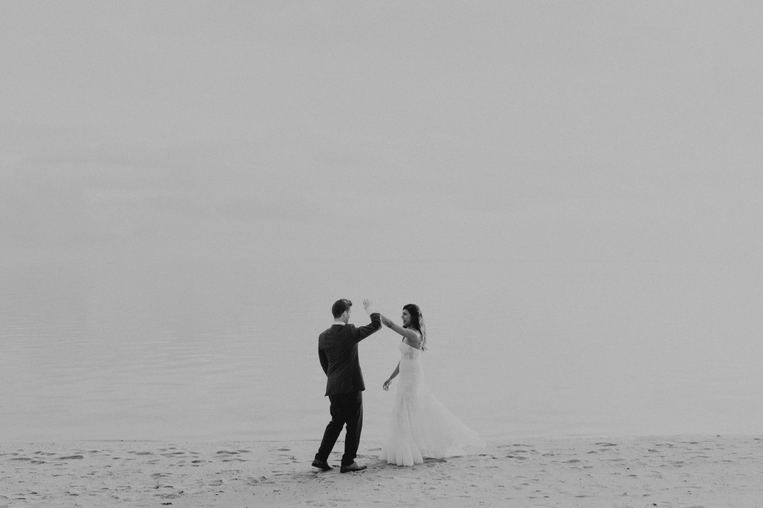 Black and white photo of couple dancing on misty beach.