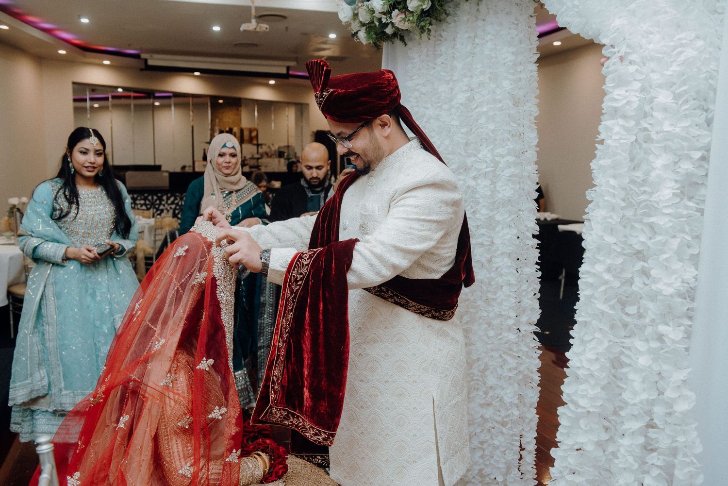 A traditional South Asian wedding ceremony with participants in ornate red and white attire exchanging ceremonial items.