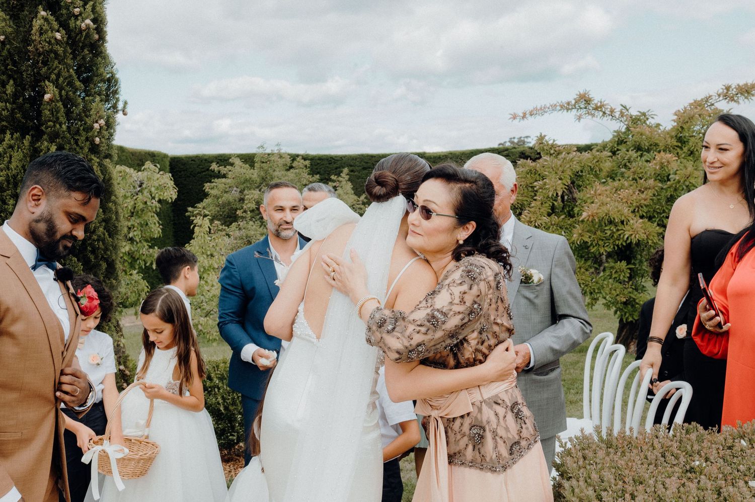 Wedding guests mingling outdoors among cypress trees during celebration.