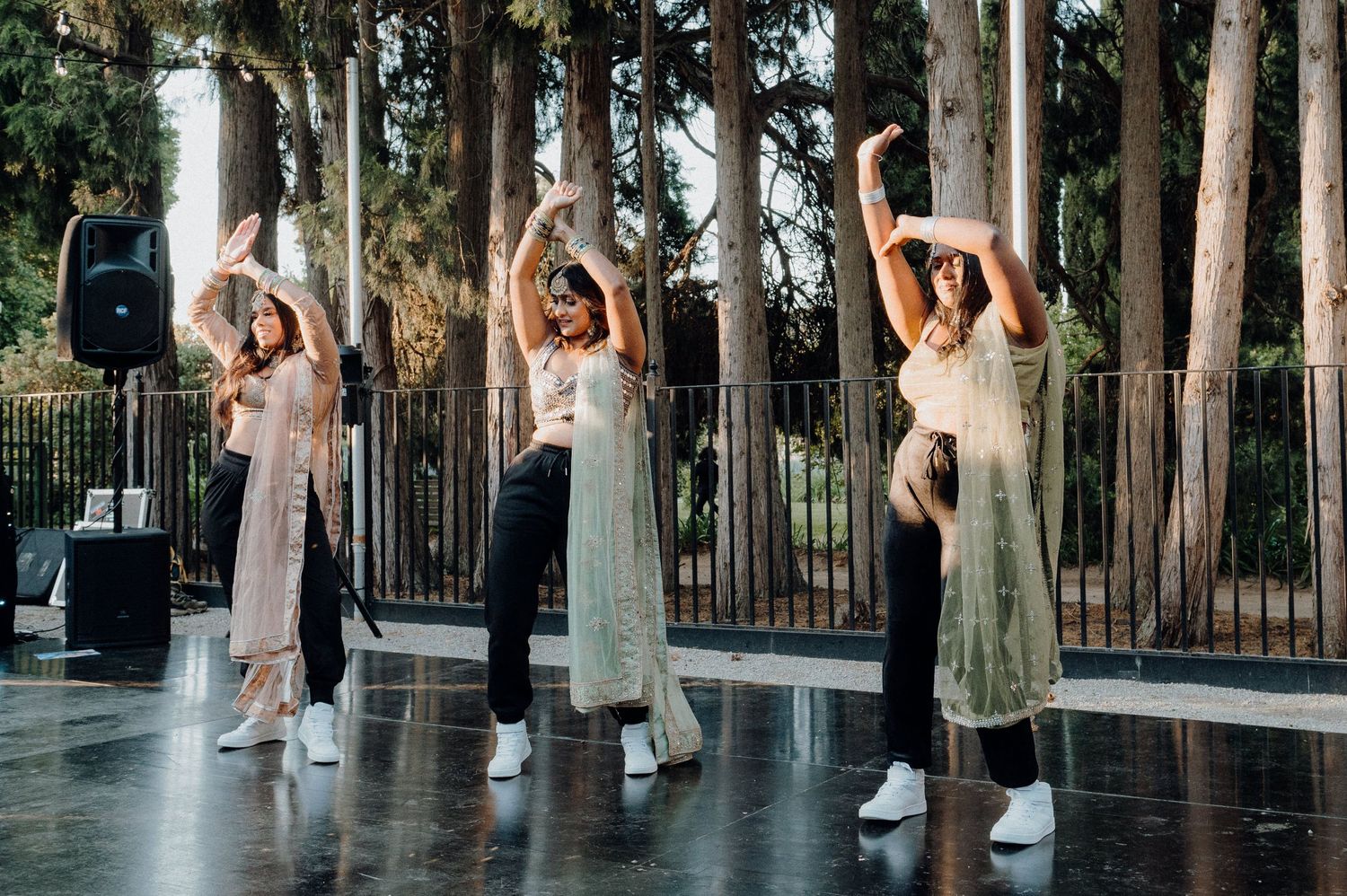 Dancers in light-colored dresses performing synchronized movements on an outdoor stage.
