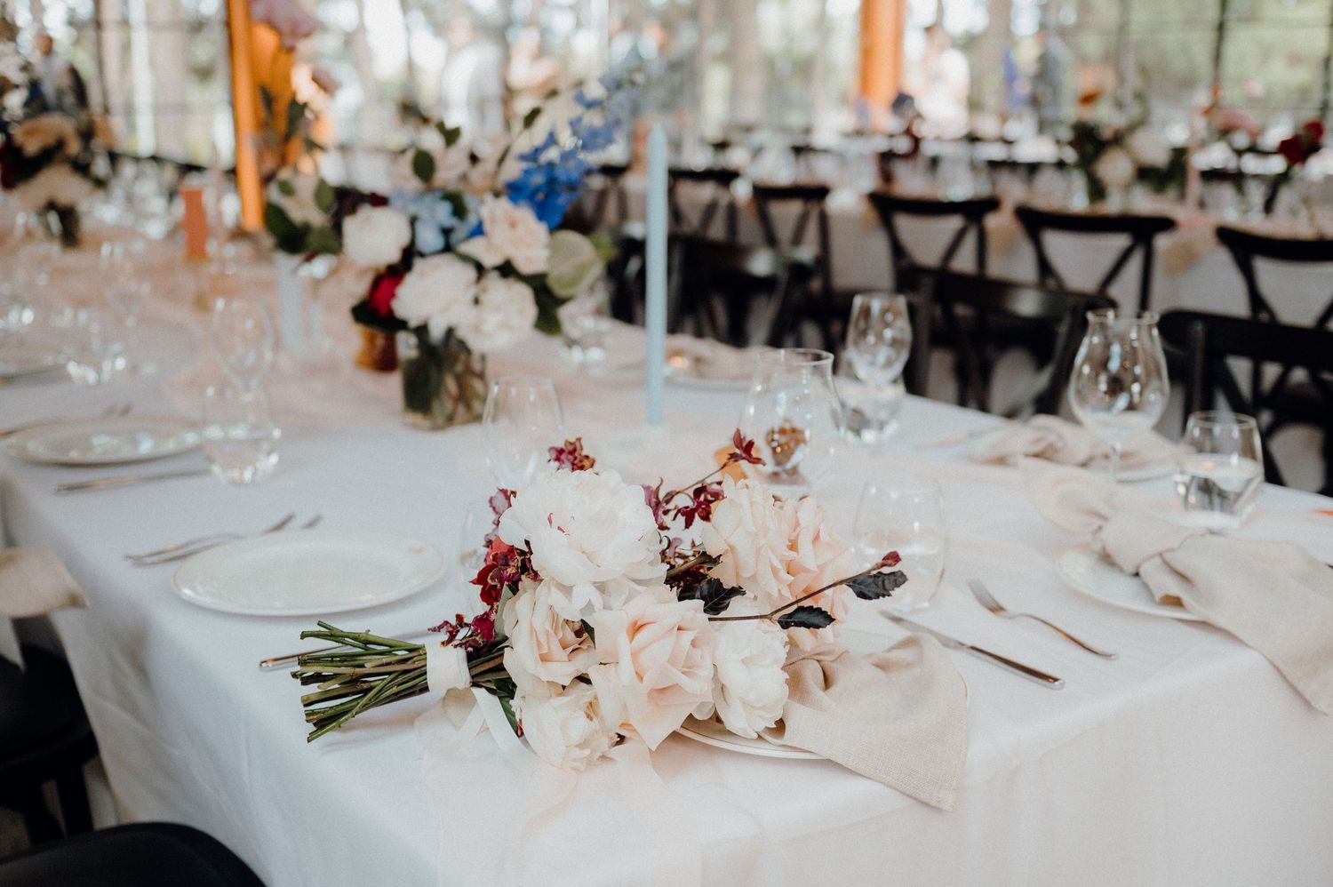 Elegant table setting with floral centerpiece and white linens at wedding reception.