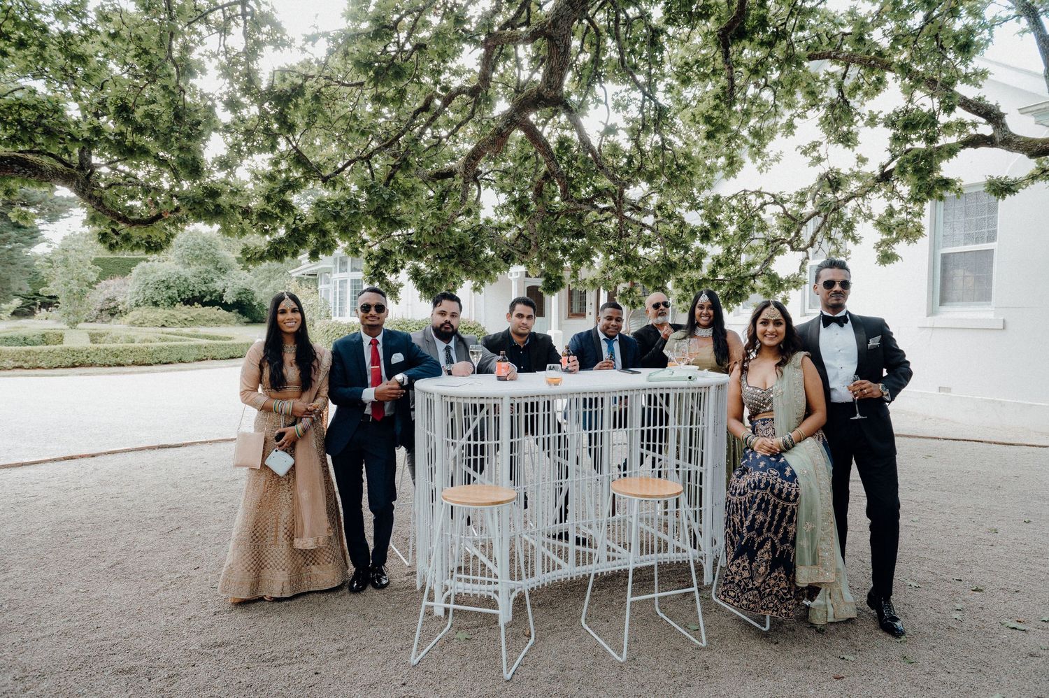 Wedding party poses with decorative white birdcage furniture at outdoor celebration.
