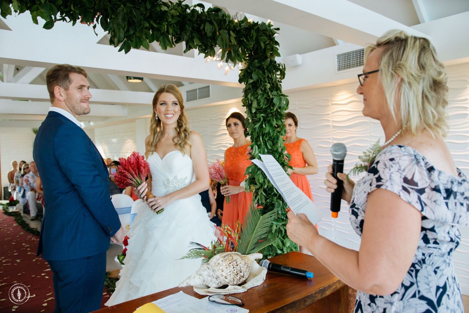 Wedding ceremony proceedings under verdant arch with celebrant and guests in attendance.