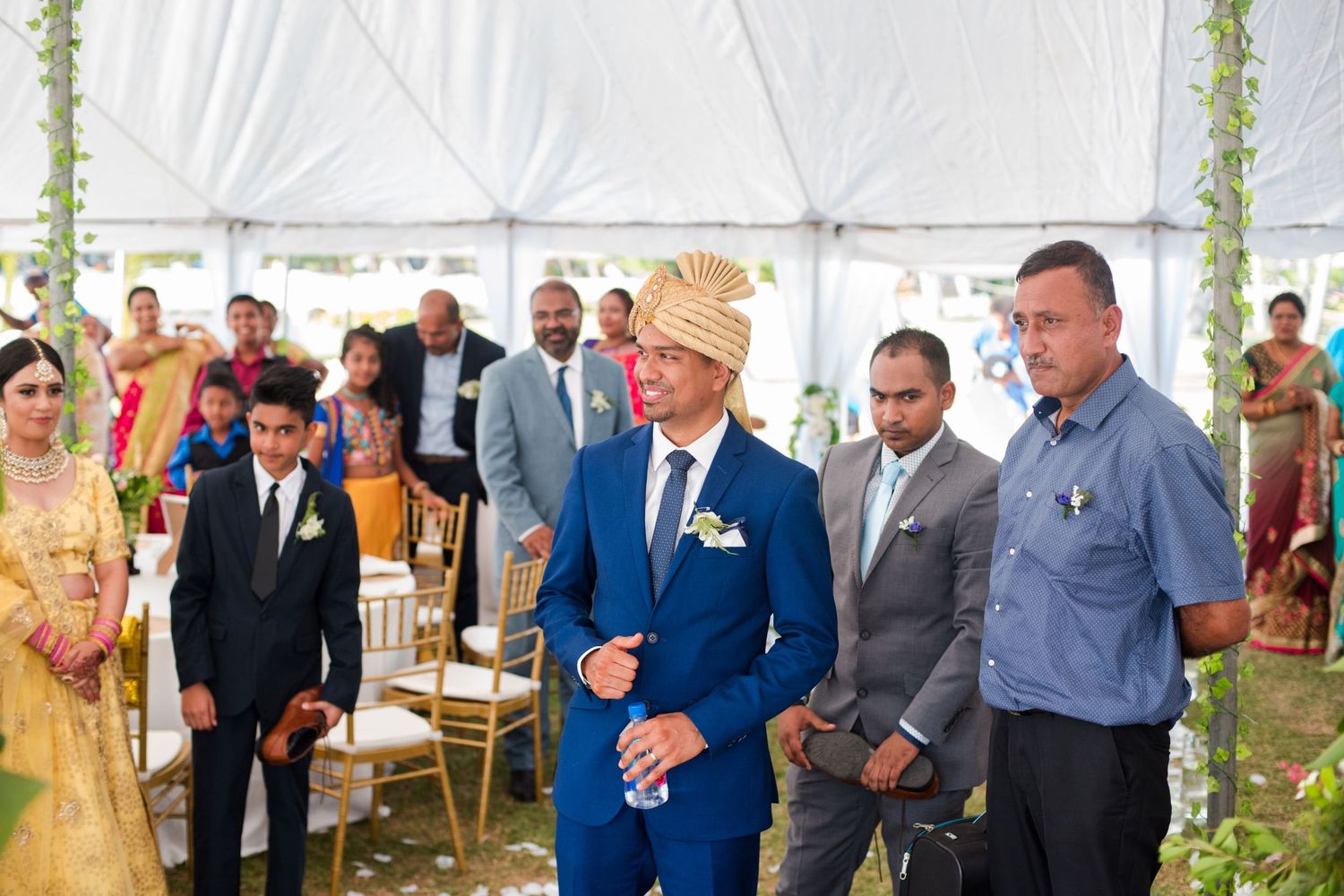 Outdoor wedding setup under a white tent with guests gathered for the ceremony.