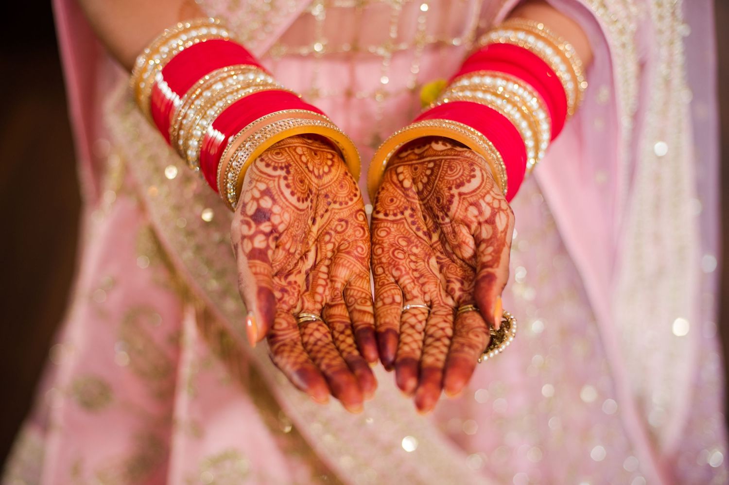 Detailed shot of intricate henna designs on hands with red wedding bangles and sparkly fabric.