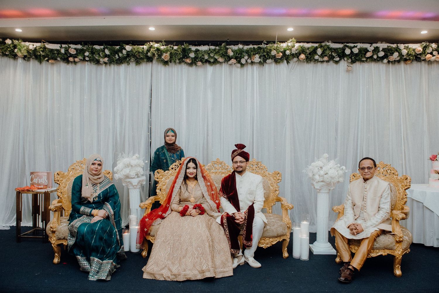 Wedding party seated on ornate chairs during traditional South Asian ceremony.