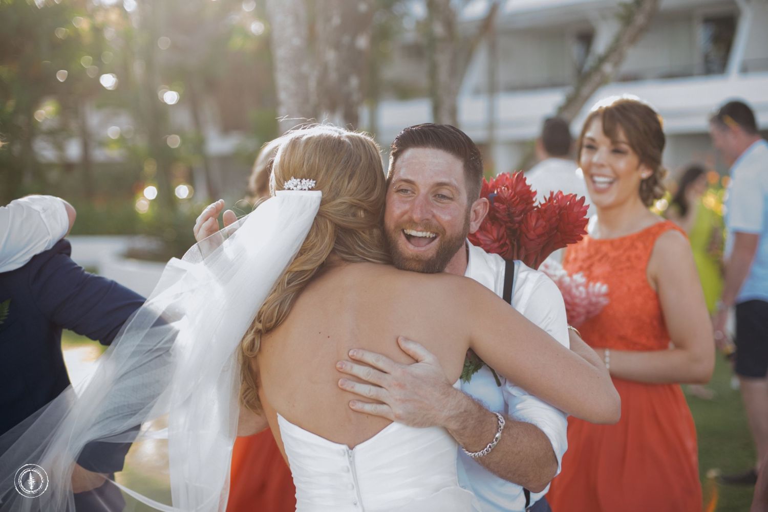 Emotional embrace during an outdoor wedding celebration with coral-colored floral accents.