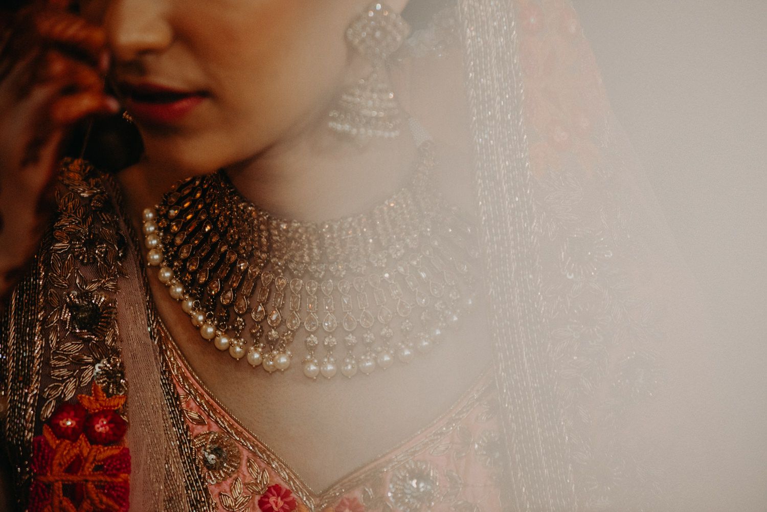 Close-up of Indian bride wearing an elaborate layered pearl and crystal bridal necklace with embroidered lehenga.