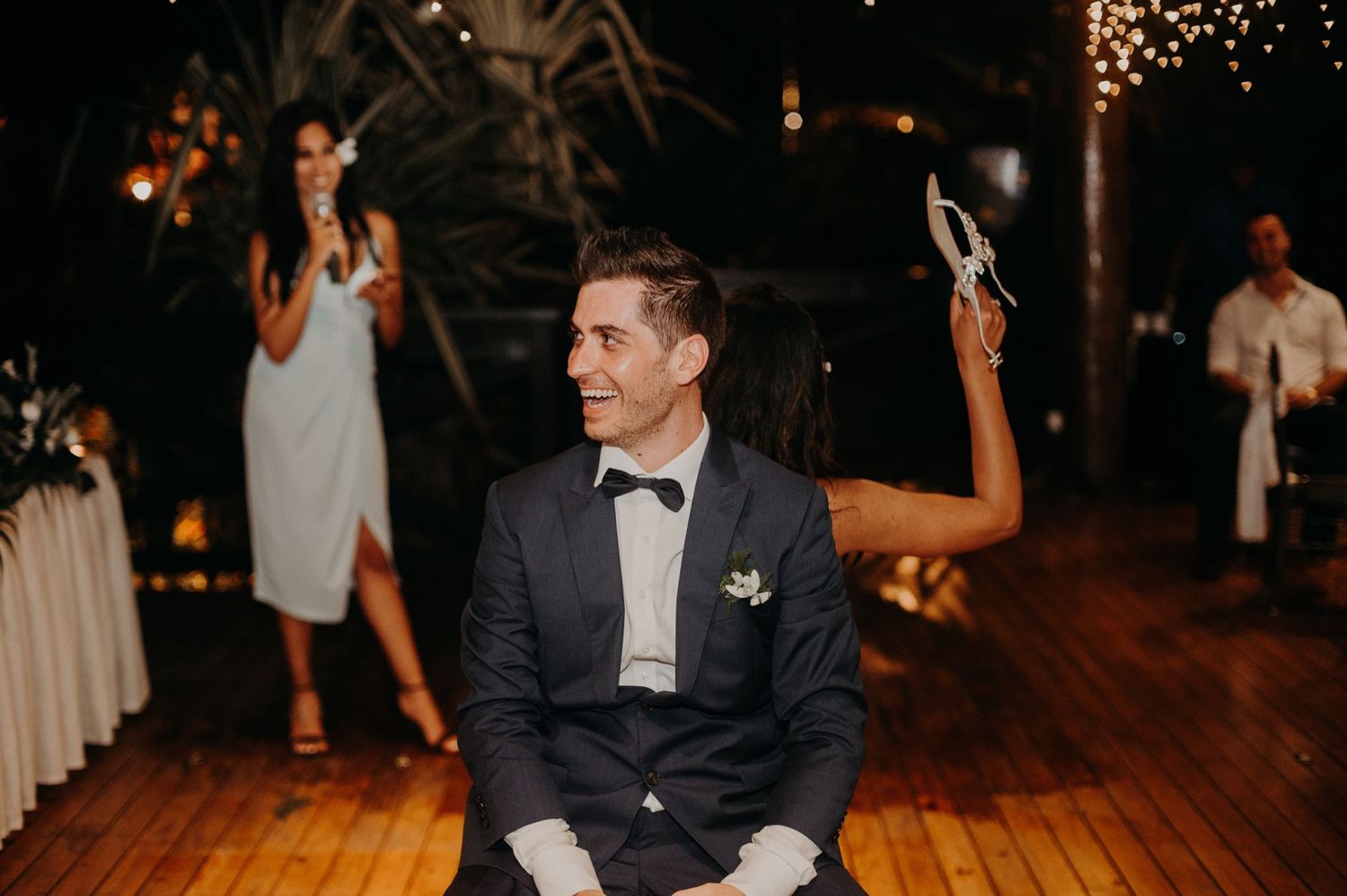 An elegant wedding celebration on a wooden dance floor with string lights and white tables.