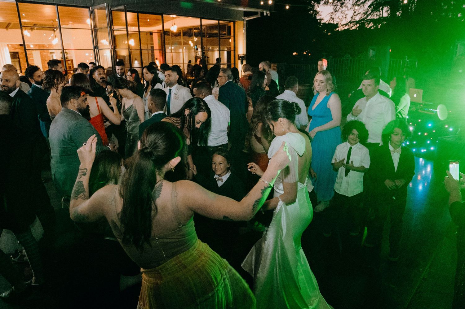 Lively wedding reception dance floor with guests celebrating under colorful lights.