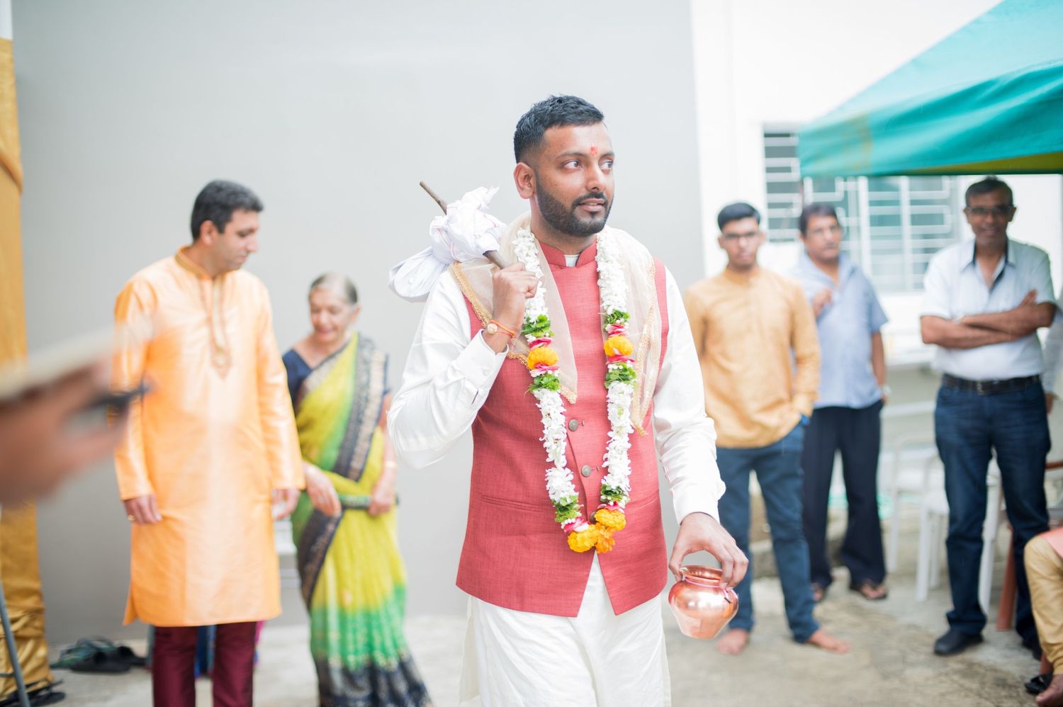 Wedding participant in red vest and white garlands during outdoor celebration.