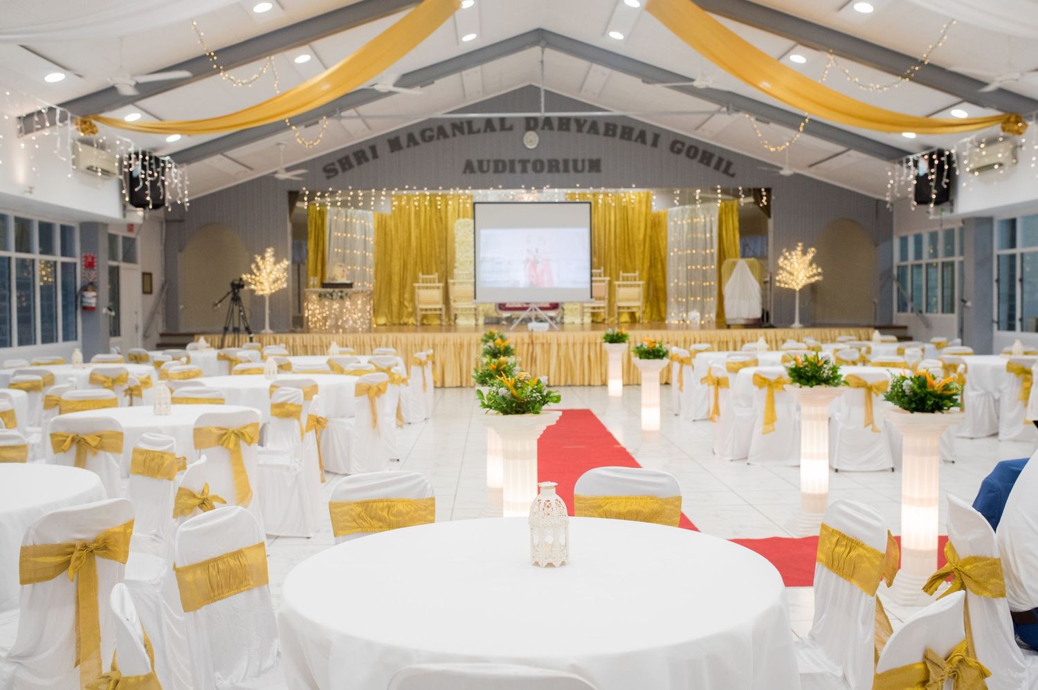 Elegant wedding reception hall decorated with white and gold drapes, round tables, and chair covers.