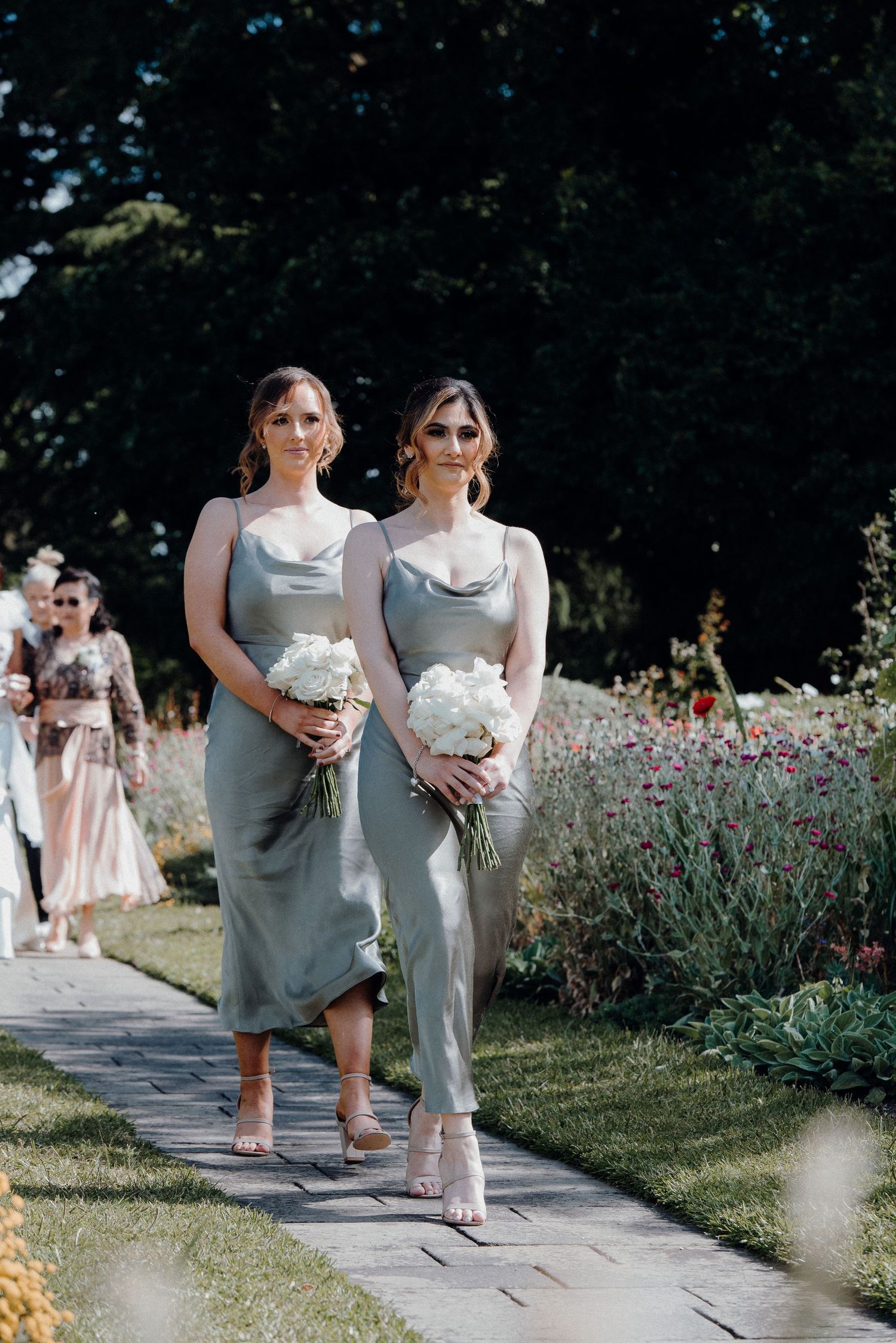 Bridesmaids in elegant gray dresses walking along garden pathway.