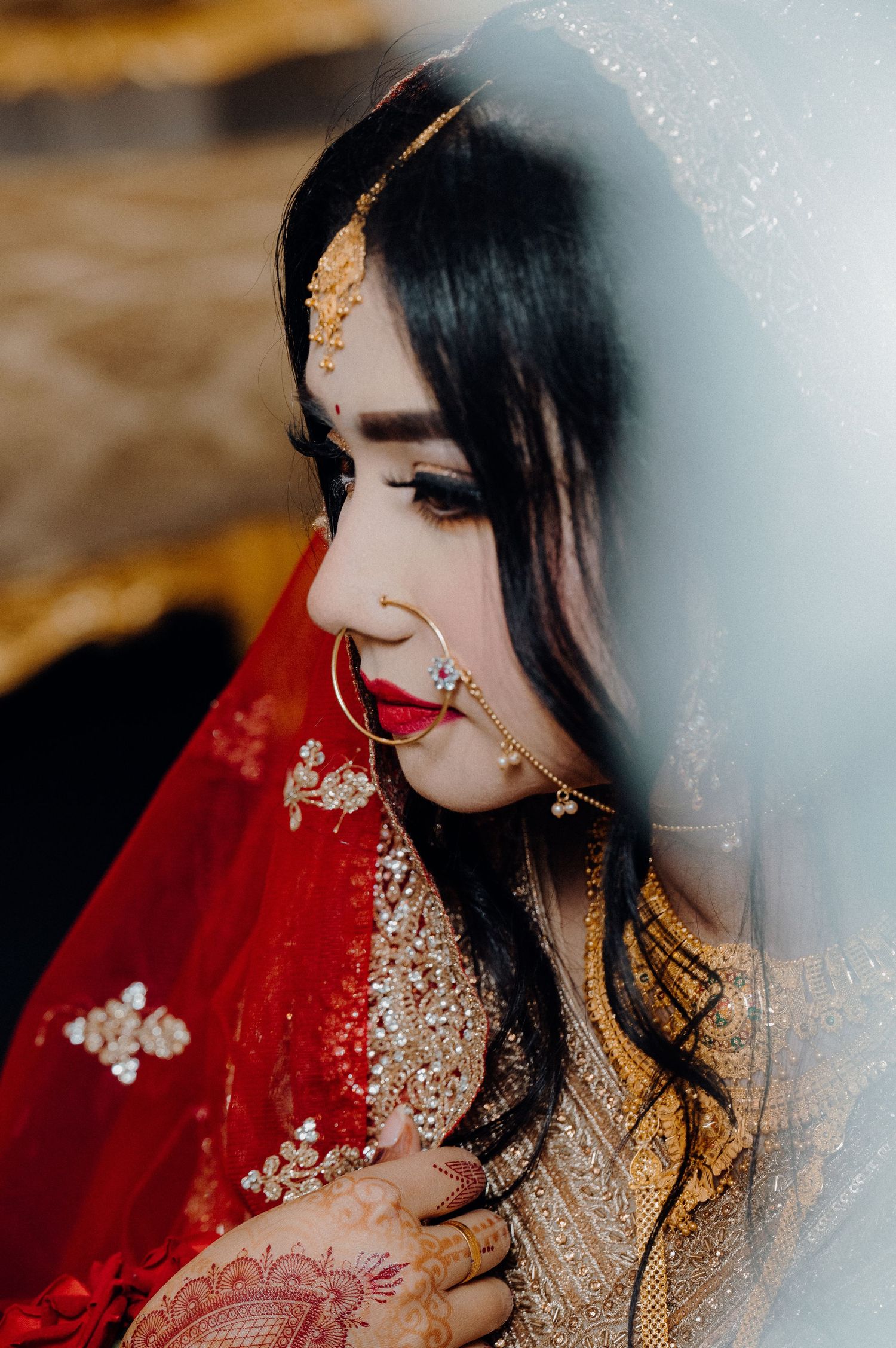 Side profile of traditional South Asian bridal attire with red veil and golden embellishments.