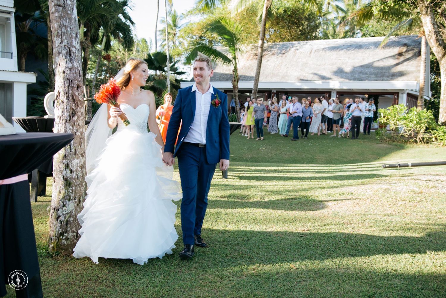 Outdoor wedding celebration on a sunny day with palm trees and green lawn.
