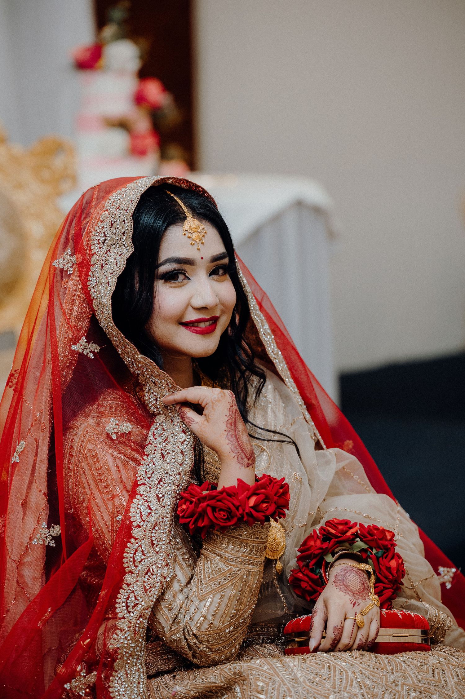 South Asian bridal portrait featuring red dupatta, golden dress and floral wrist accessories.