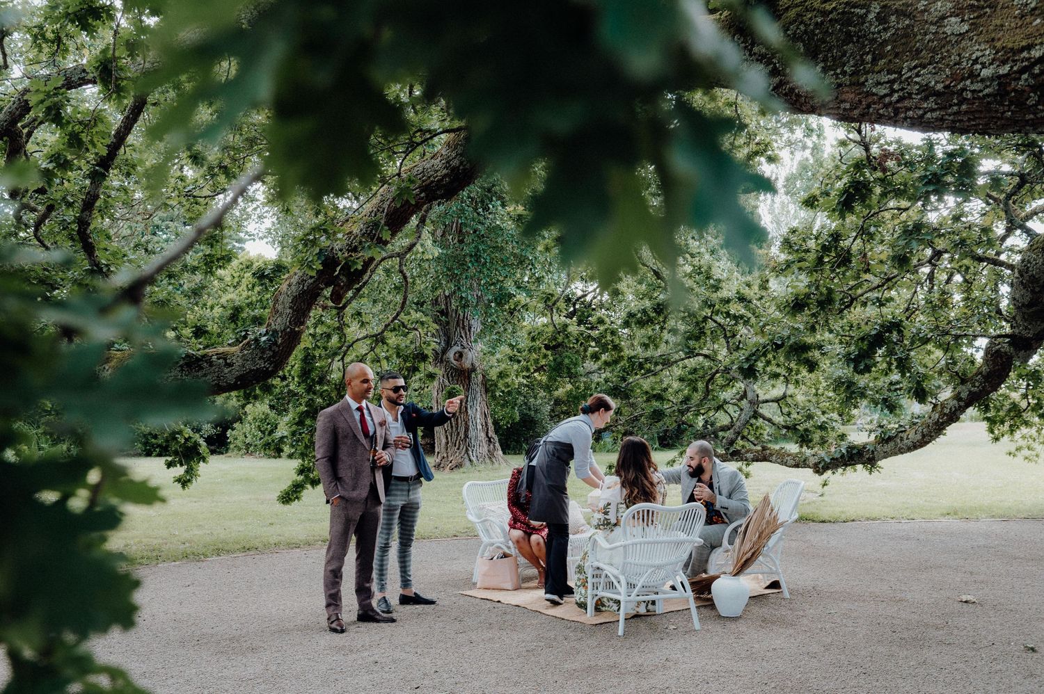 Friends gather around an elegant white table beneath a blooming tree in a garden setting.