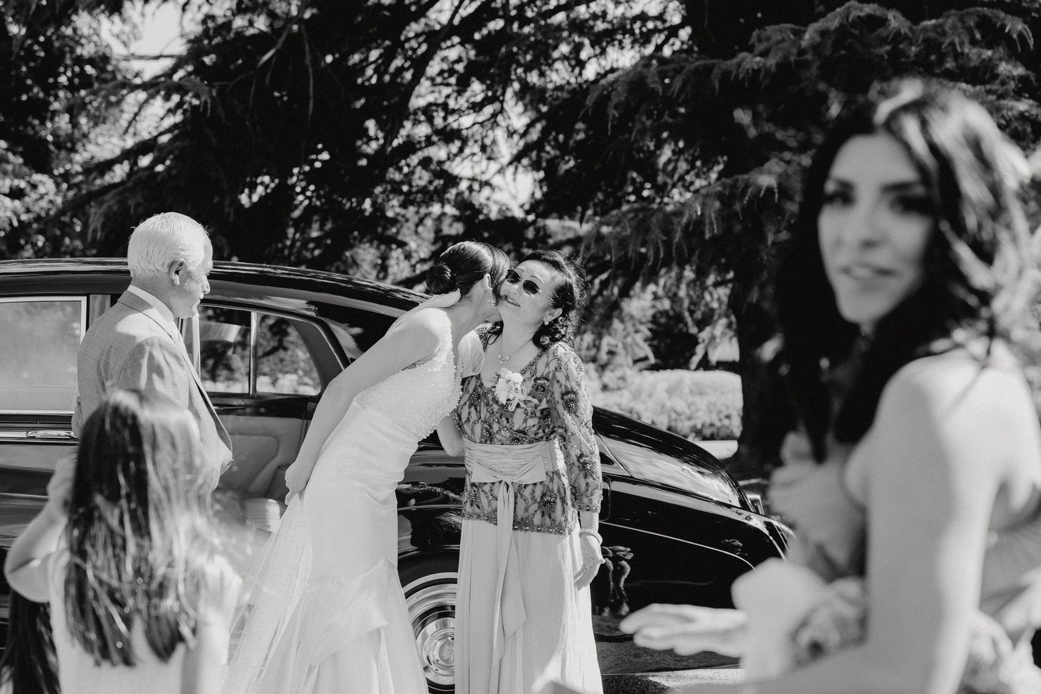 Black and white photo of wedding guests gathering around vintage car.