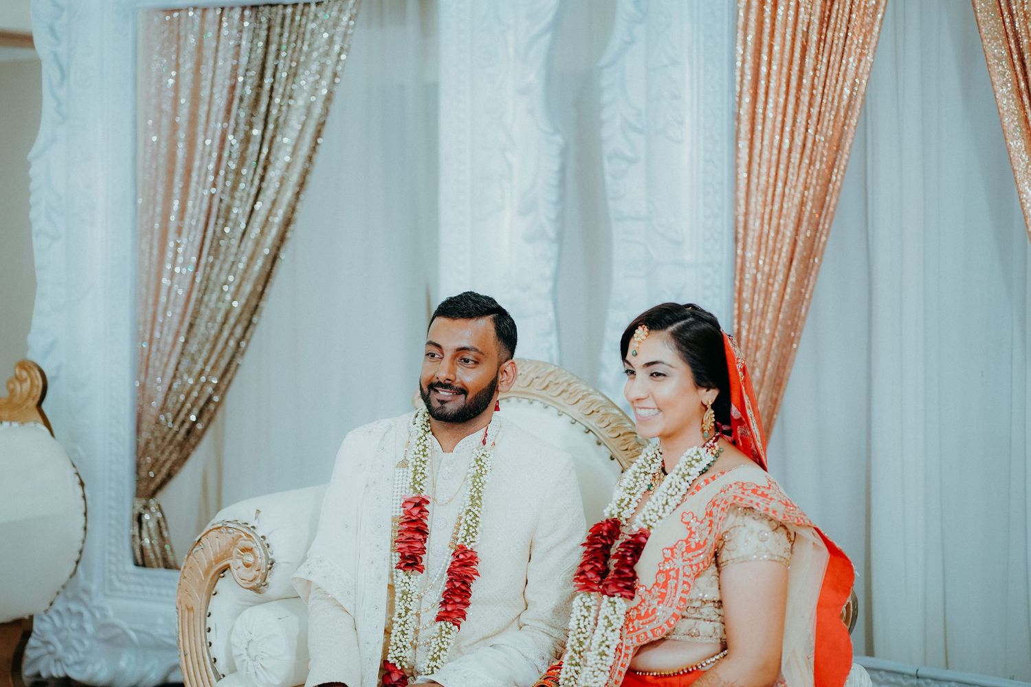 A couple seated during their traditional wedding ceremony with sparkly backdrop and decor.