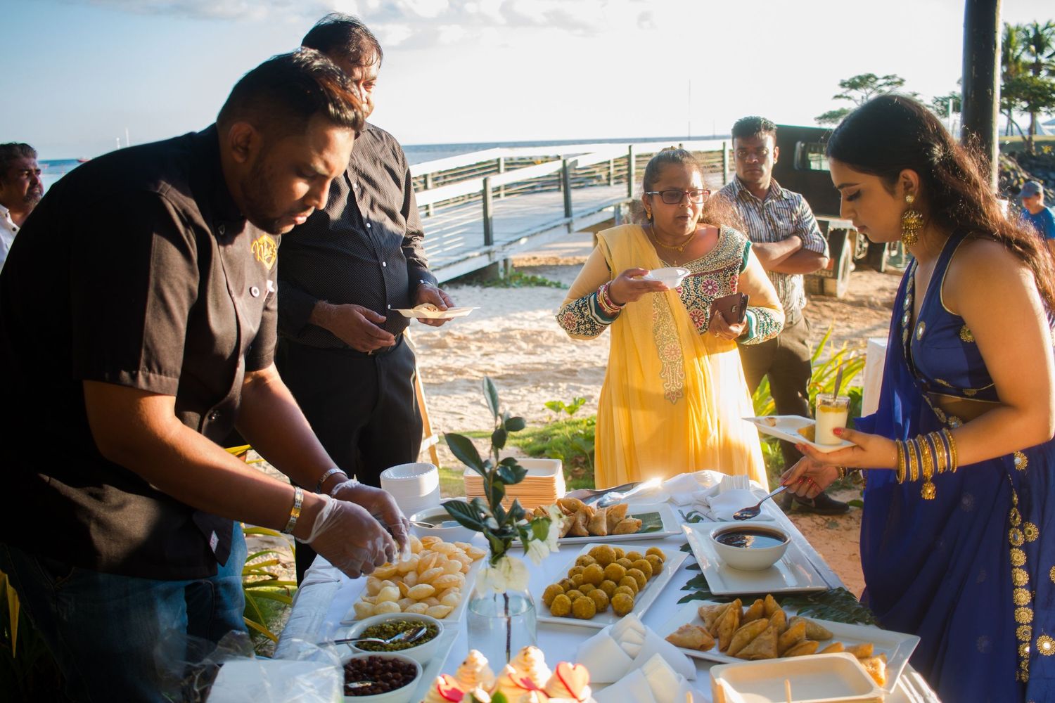 Guests serve themselves from a buffet spread at an outdoor waterfront celebration.