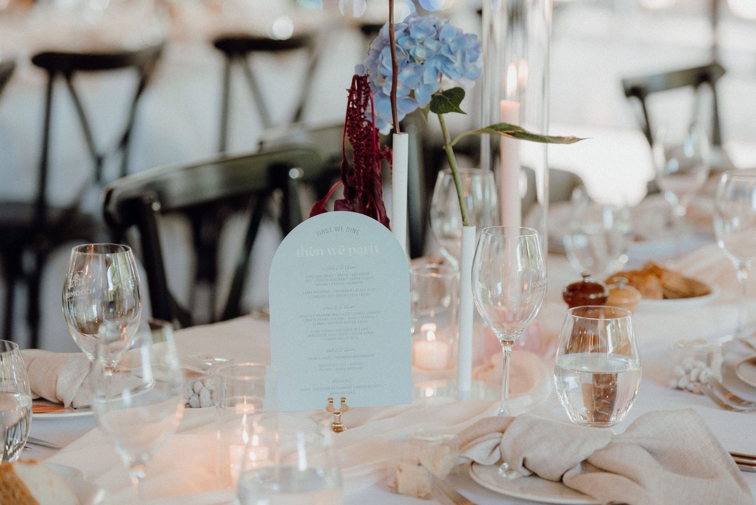 Wedding table decor featuring blue menu card, wine glasses and candlelight.