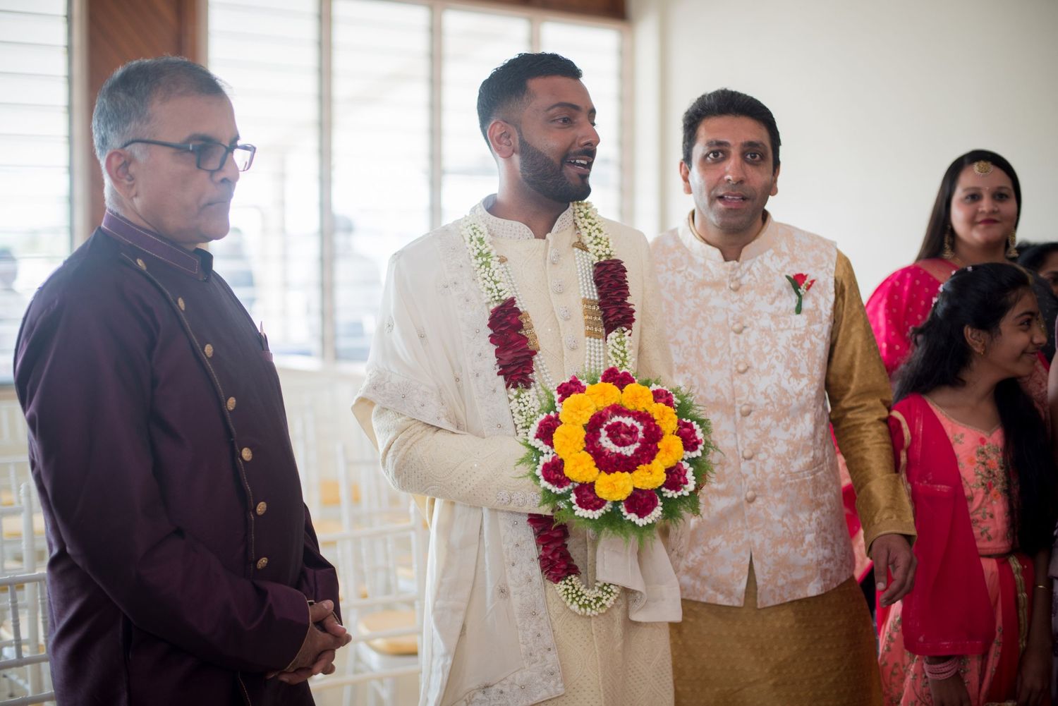 Guests in traditional Indian attire gather during a formal wedding ceremony with floral decorations.