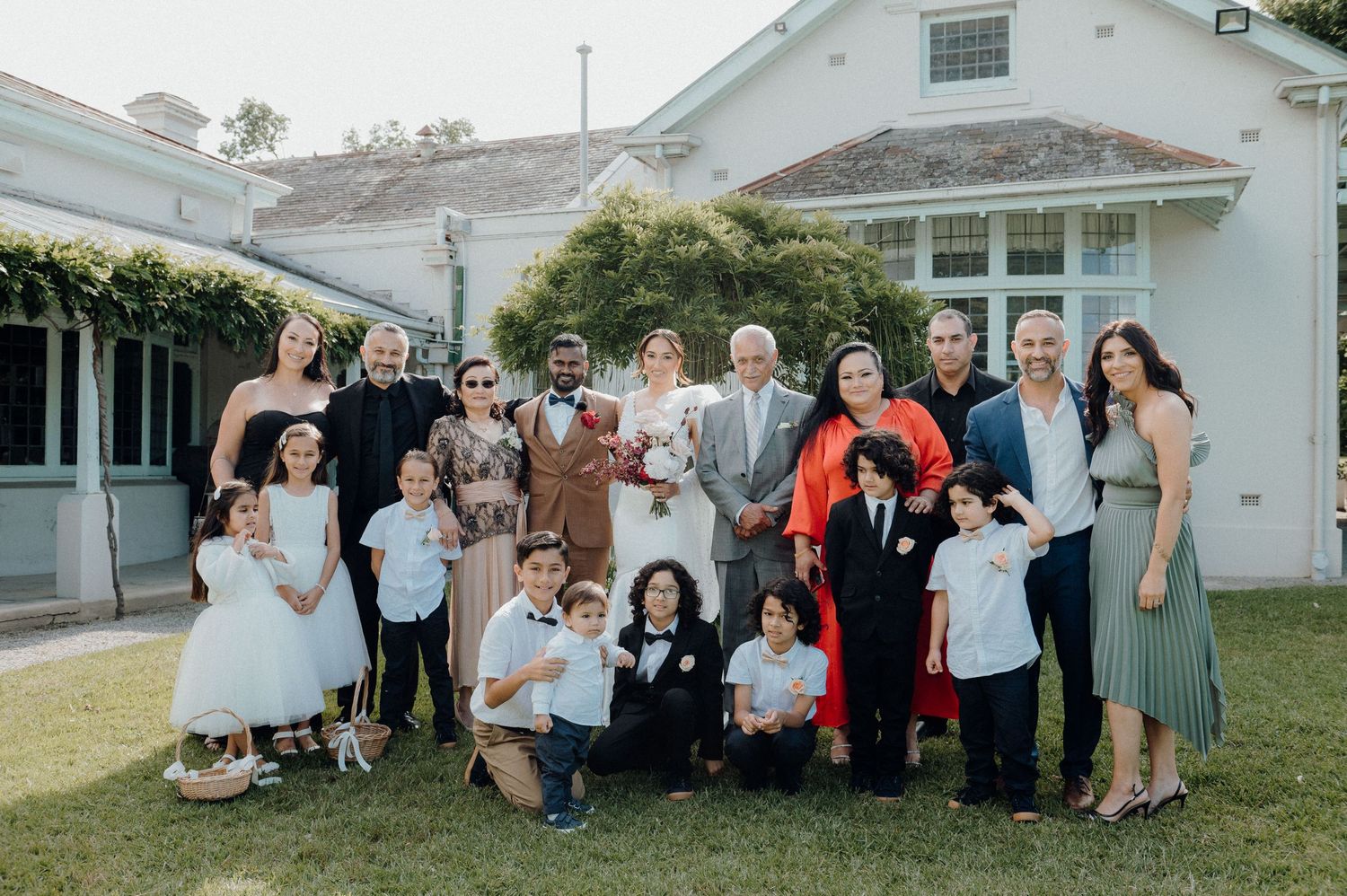 Extended family gathering for a group photo outside a white house with blue trim.