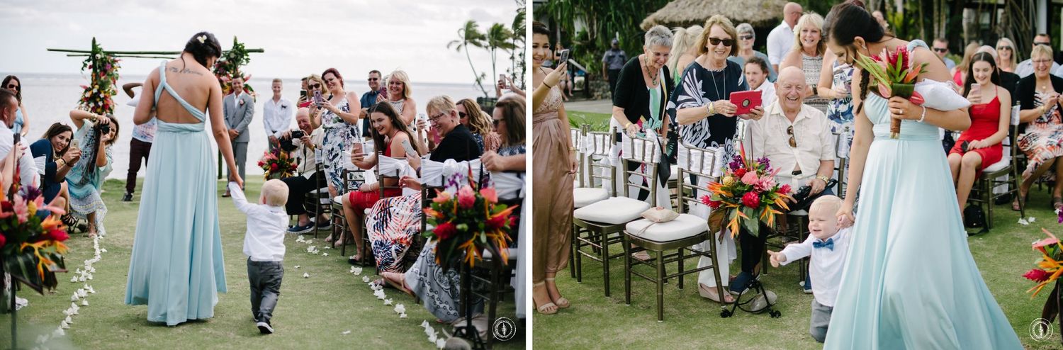 Wedding party in light blue dresses walking down an outdoor aisle lined with guests.