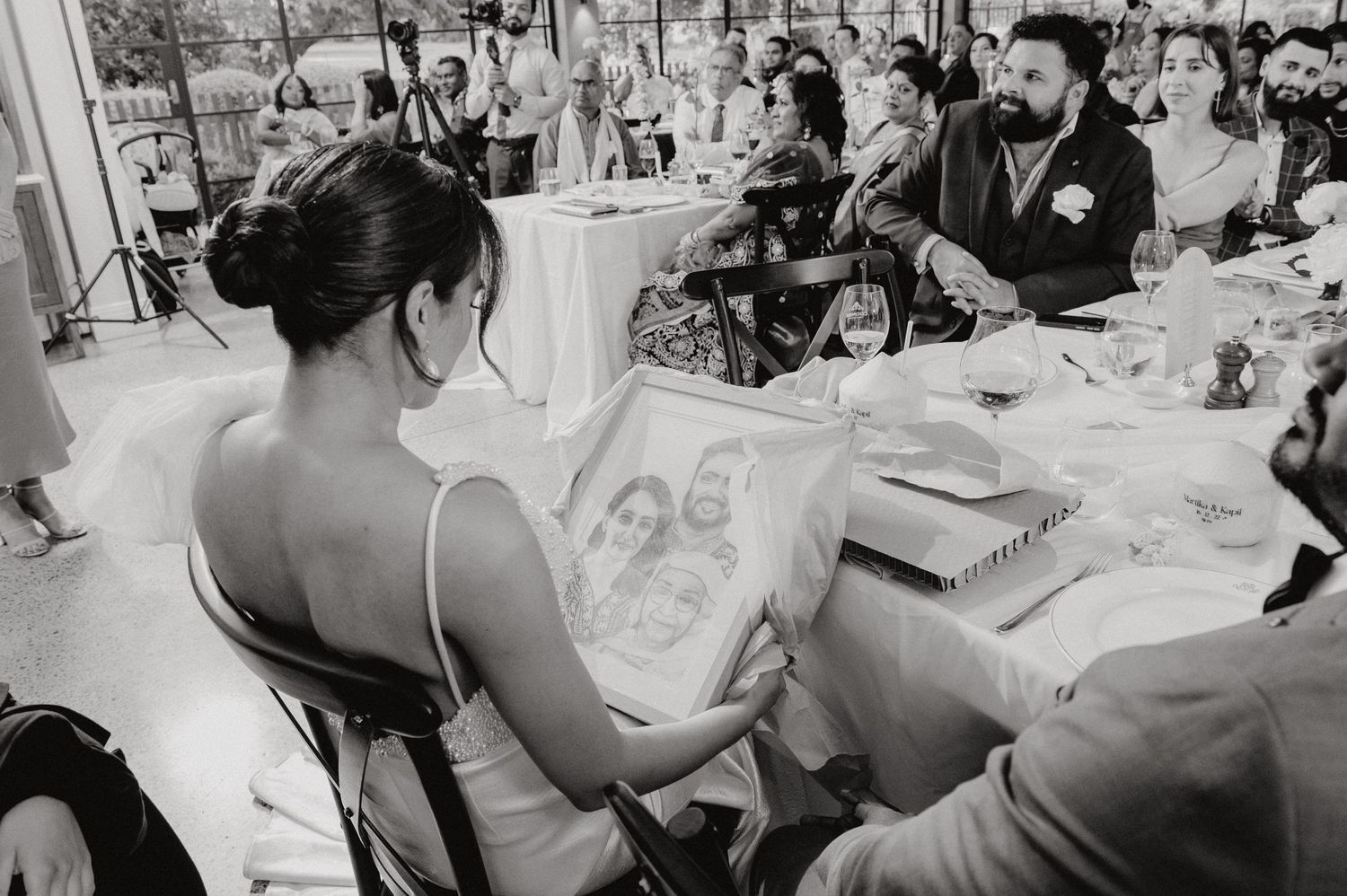 Black and white photo of reception guest reading from book at wedding celebration.