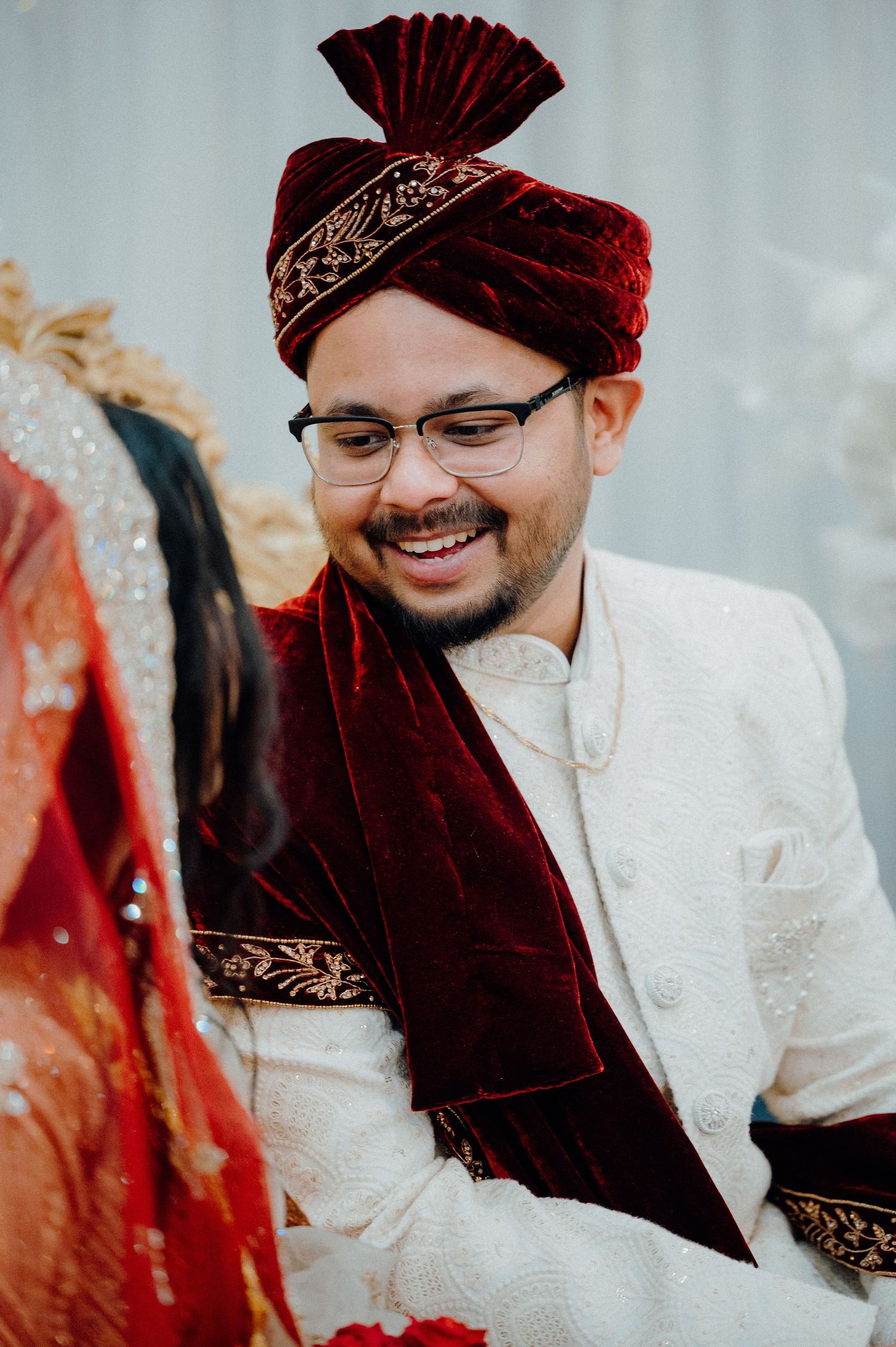 Groom wearing traditional maroon velvet turban and white sherwani during South Asian wedding ceremony.