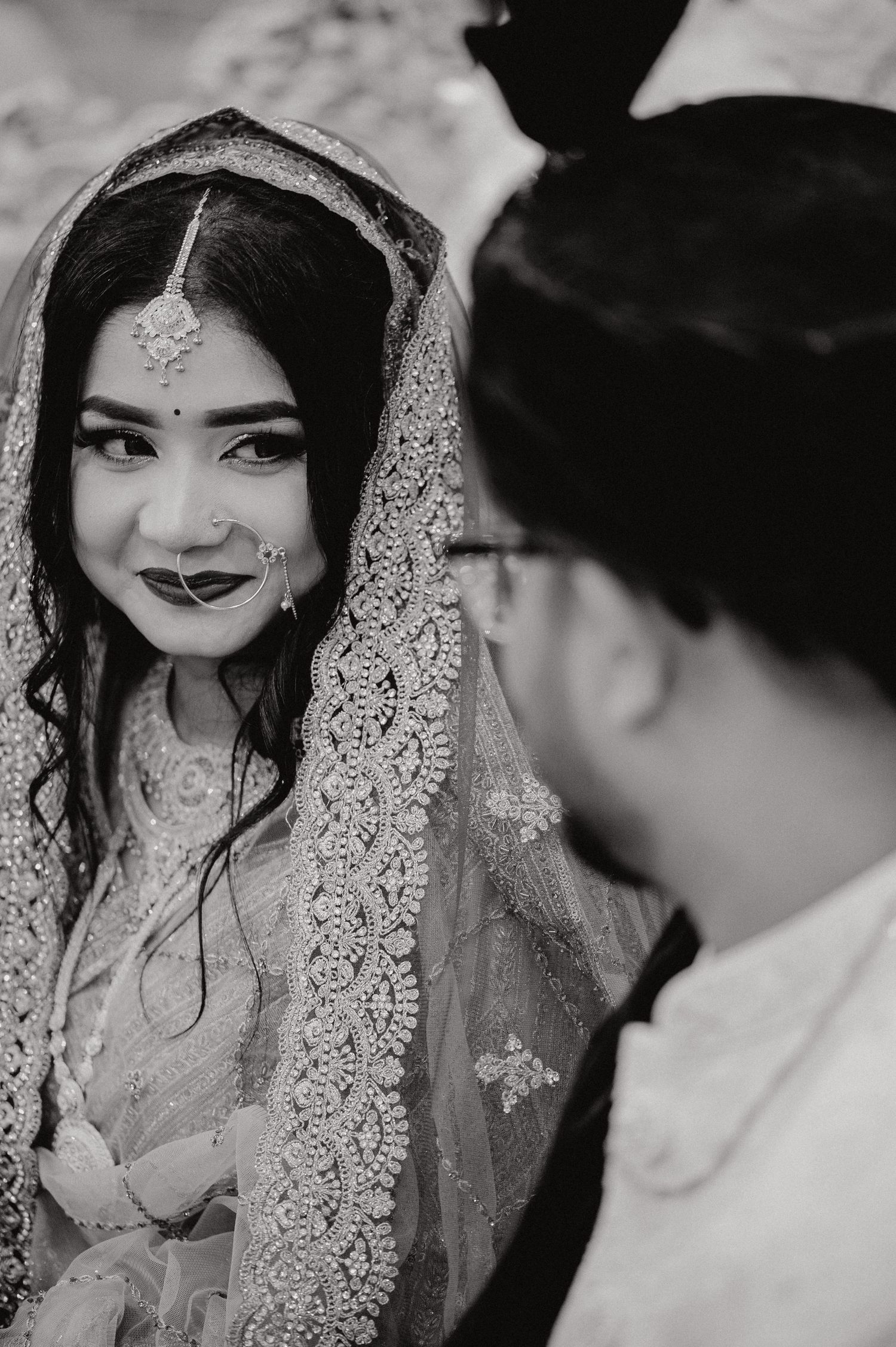 Black and white portrait of a bride in traditional South Asian wedding attire with delicate lace veil.