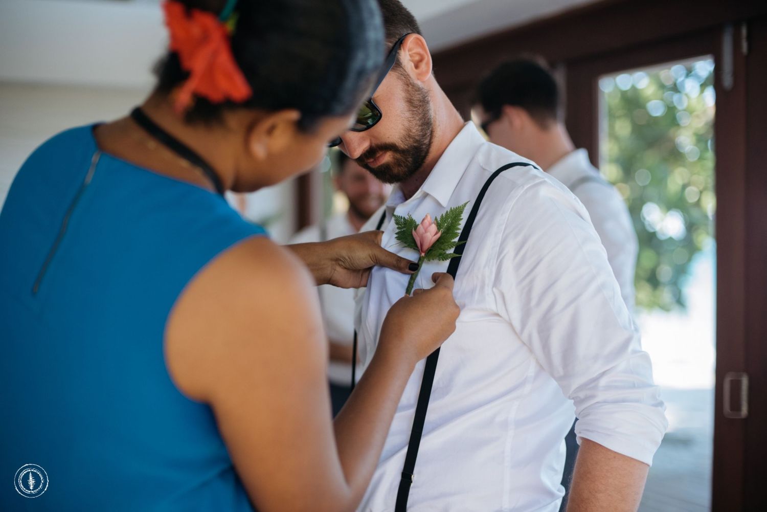A boutonniere is being pinned onto a white dress shirt during wedding preparations.
