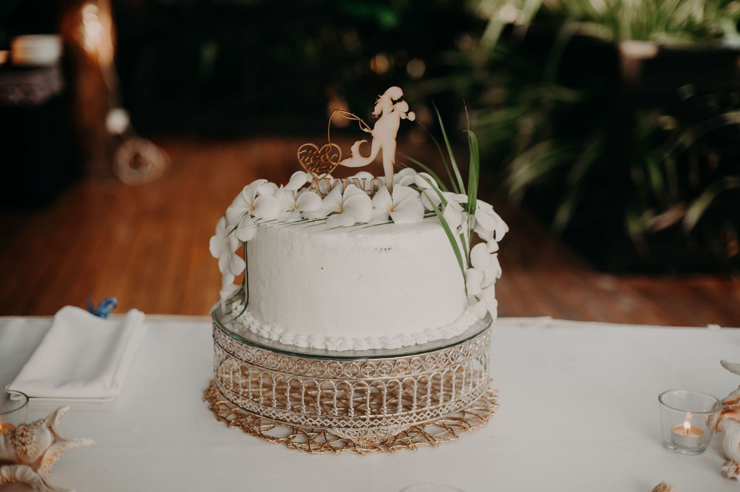 White wedding cake with floral decorations displayed on rustic burlap stand.