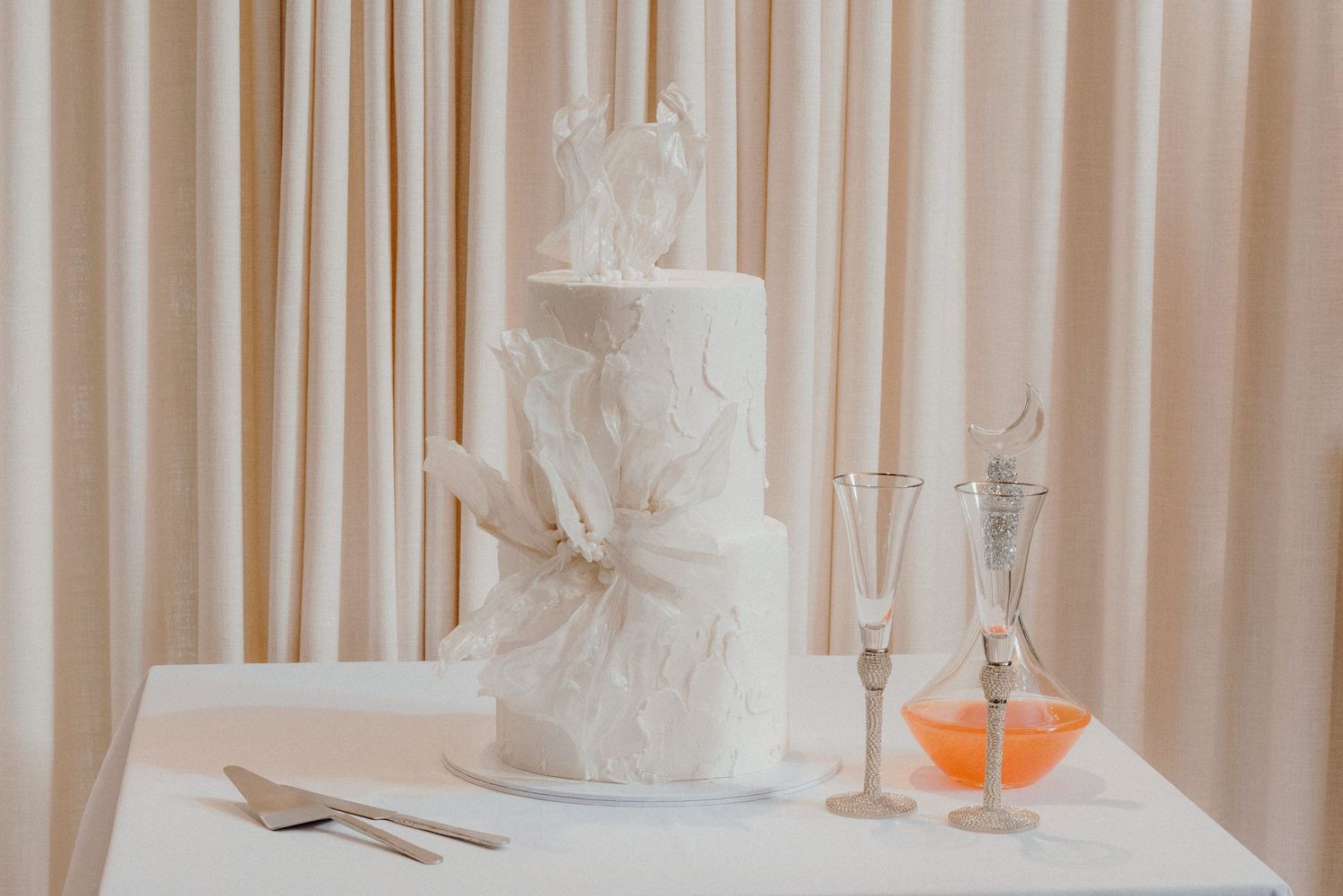 Elegant white wedding cake with delicate lace details displayed next to champagne glasses.