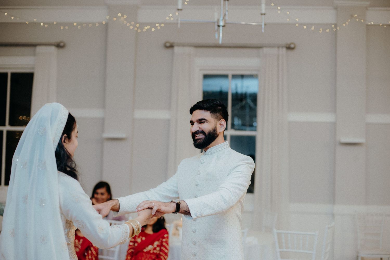 Wedding ceremony with couple exchanging rings in an elegant white-themed indoor setting.
