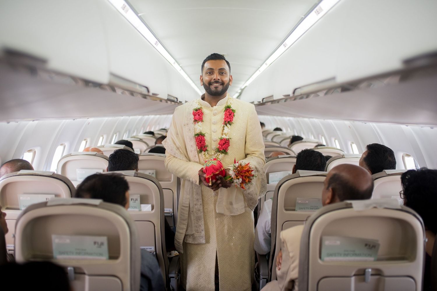 View down the aisle of an airplane cabin with passenger wearing traditional Indian wedding attire.