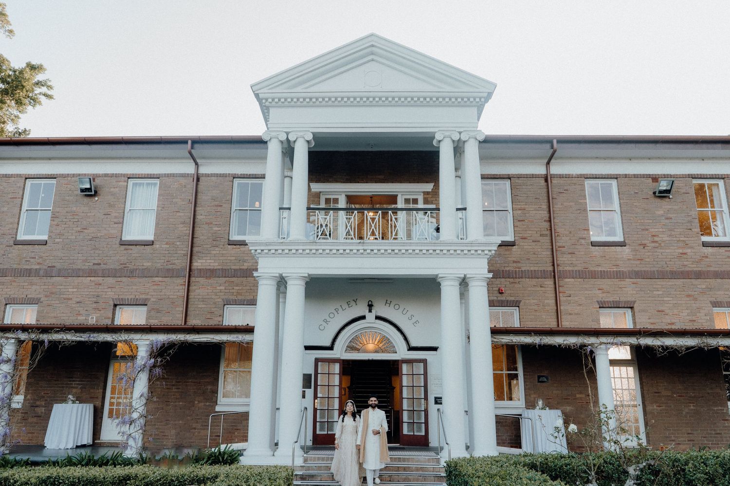 Historic Southern mansion with two-story white columns and brick facade photographed during a wedding celebration.