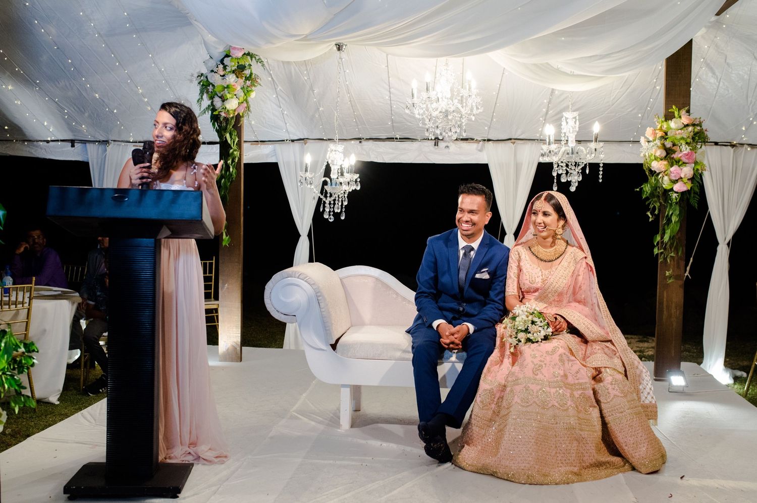 Wedding ceremony setup with elegant white decor, chandeliers and floral arrangements.