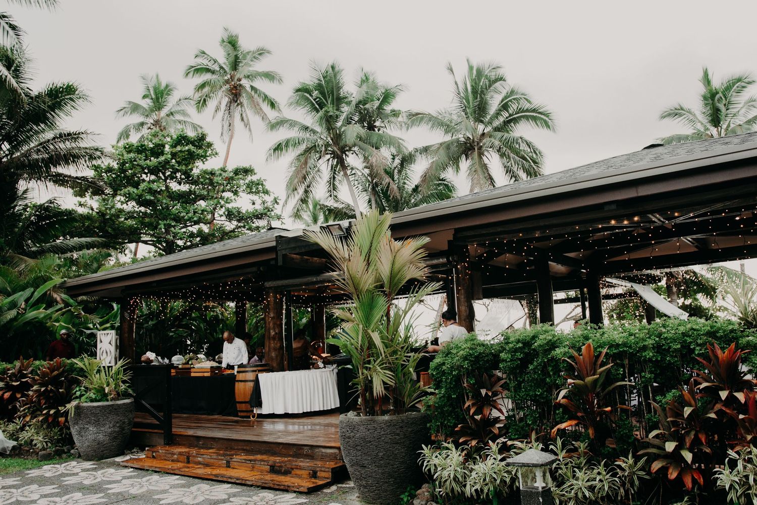 Tropical wedding venue with palm trees and wooden deck featuring covered dining area and elegant decor.