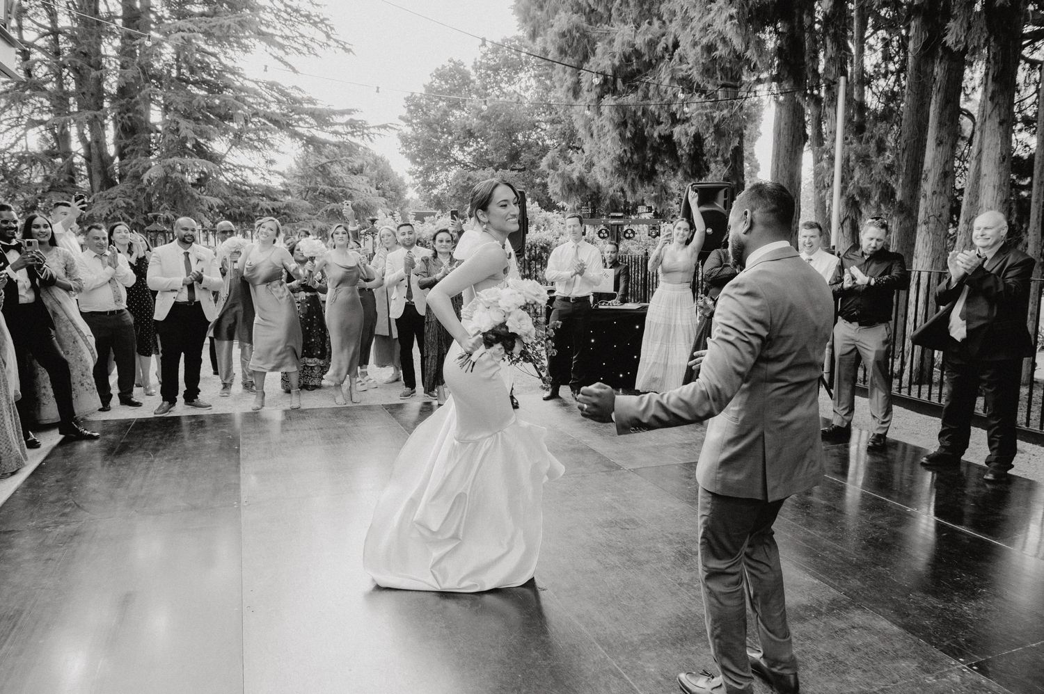 Black and white photo of a couple sharing their first dance on a covered outdoor pavilion.