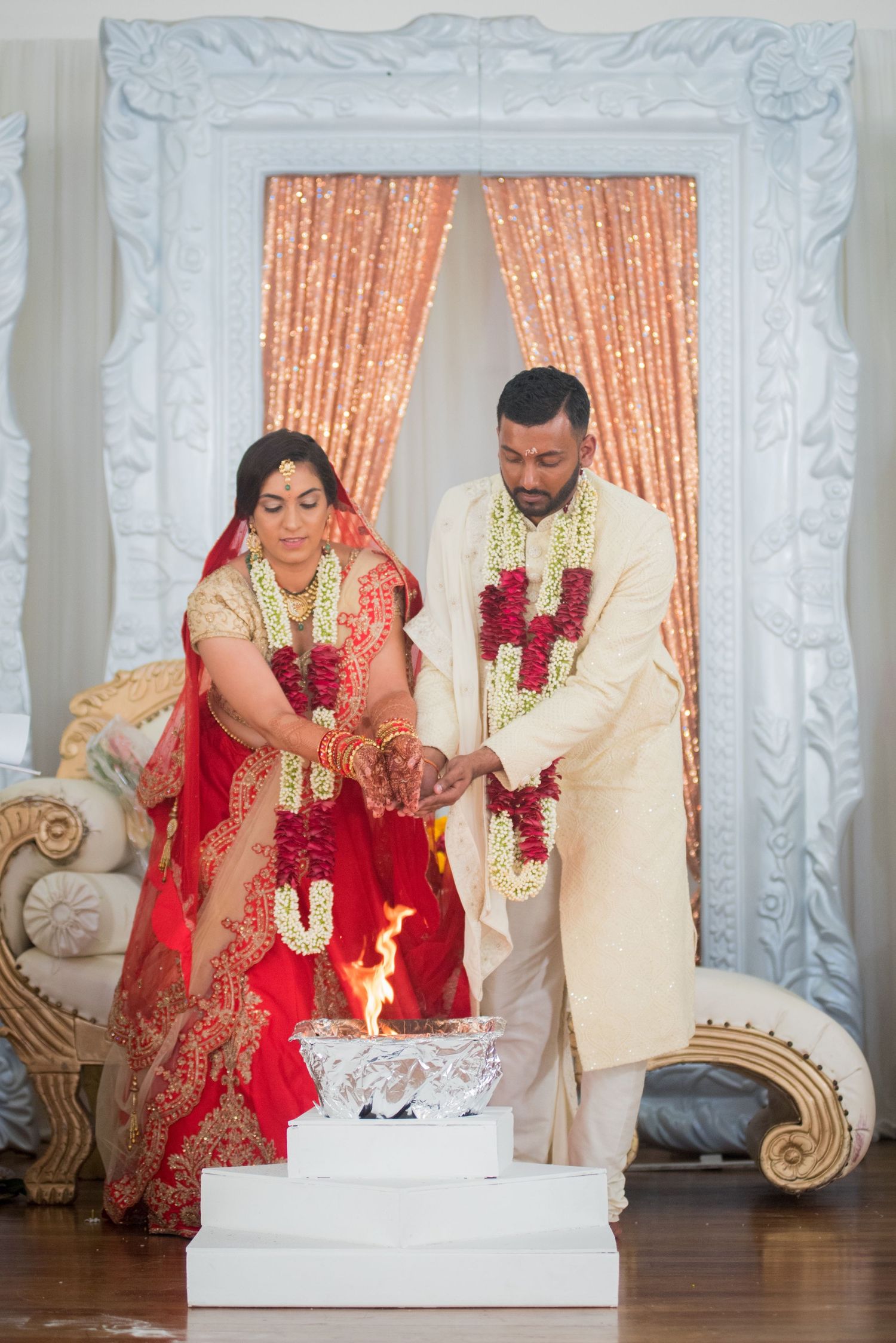 A couple in traditional Indian wedding attire performing a ritual ceremony with candles.