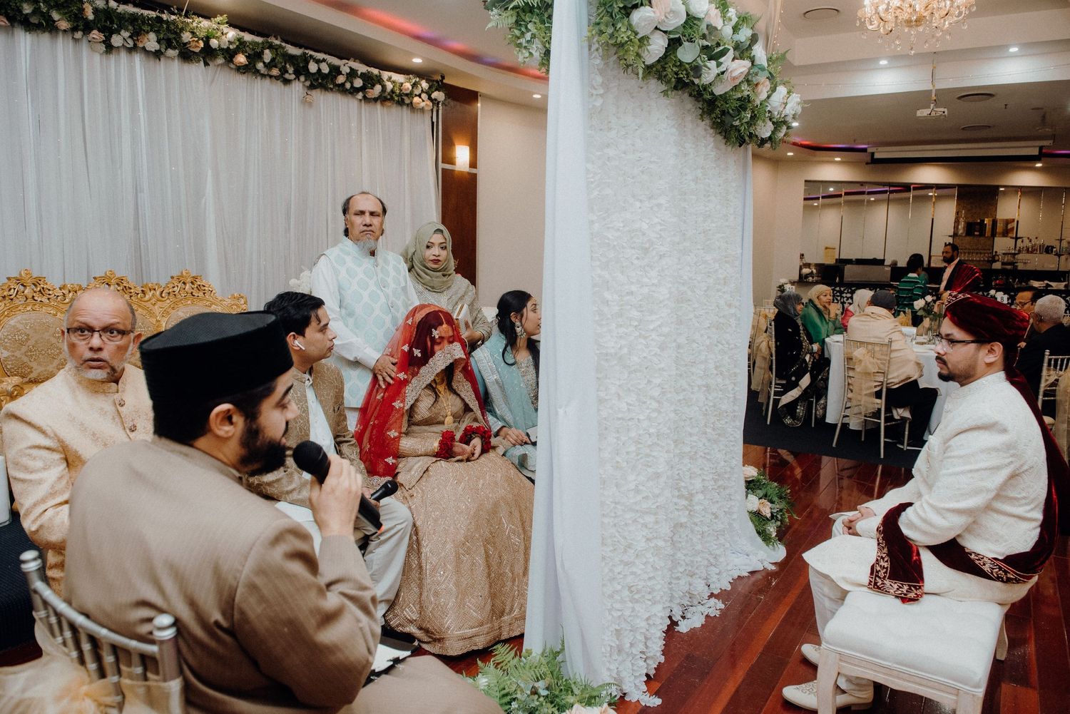 Wedding ceremony setup with white pillars and floral decorations in an indoor venue.