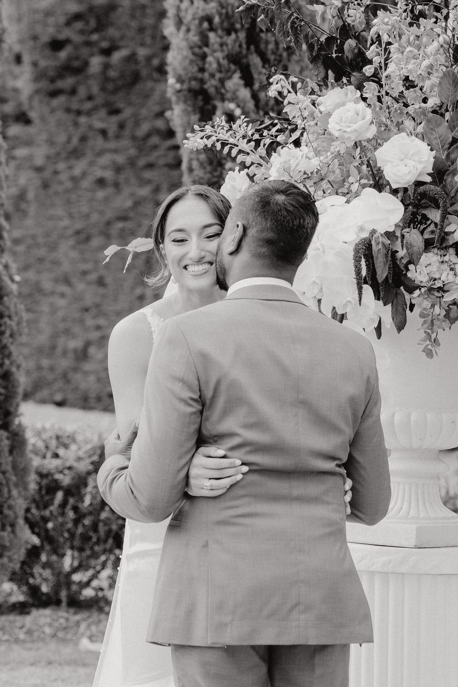 Black and white romantic moment captured during wedding ceremony beside floral arrangements.