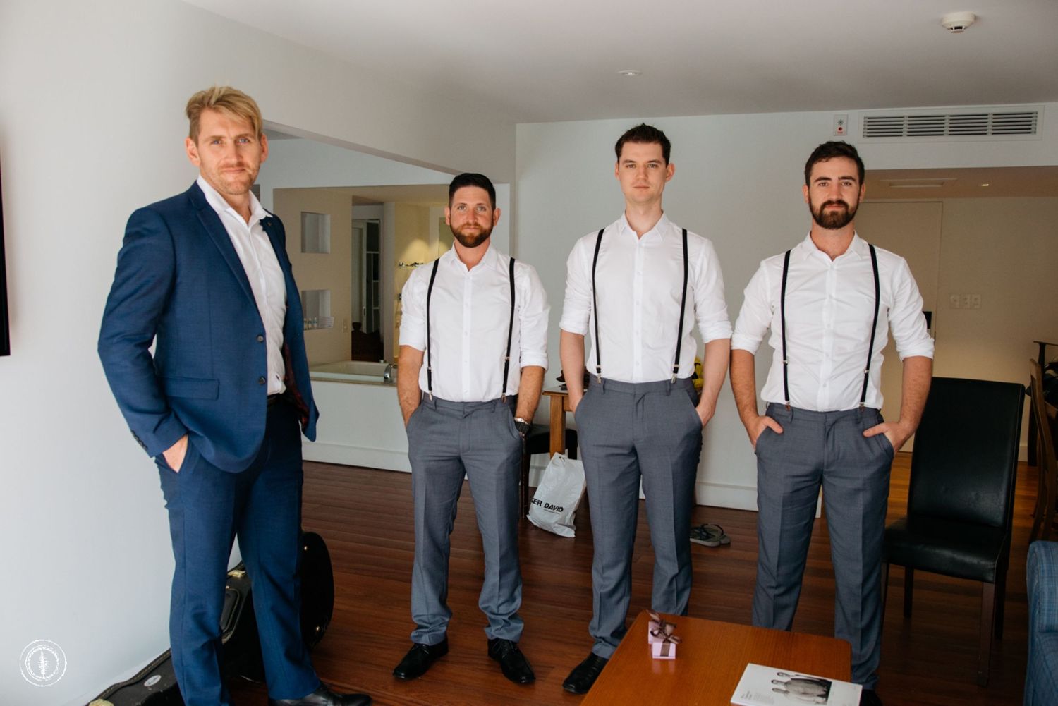 Groomsmen in suspenders and dress shirts pose with best man in navy suit.