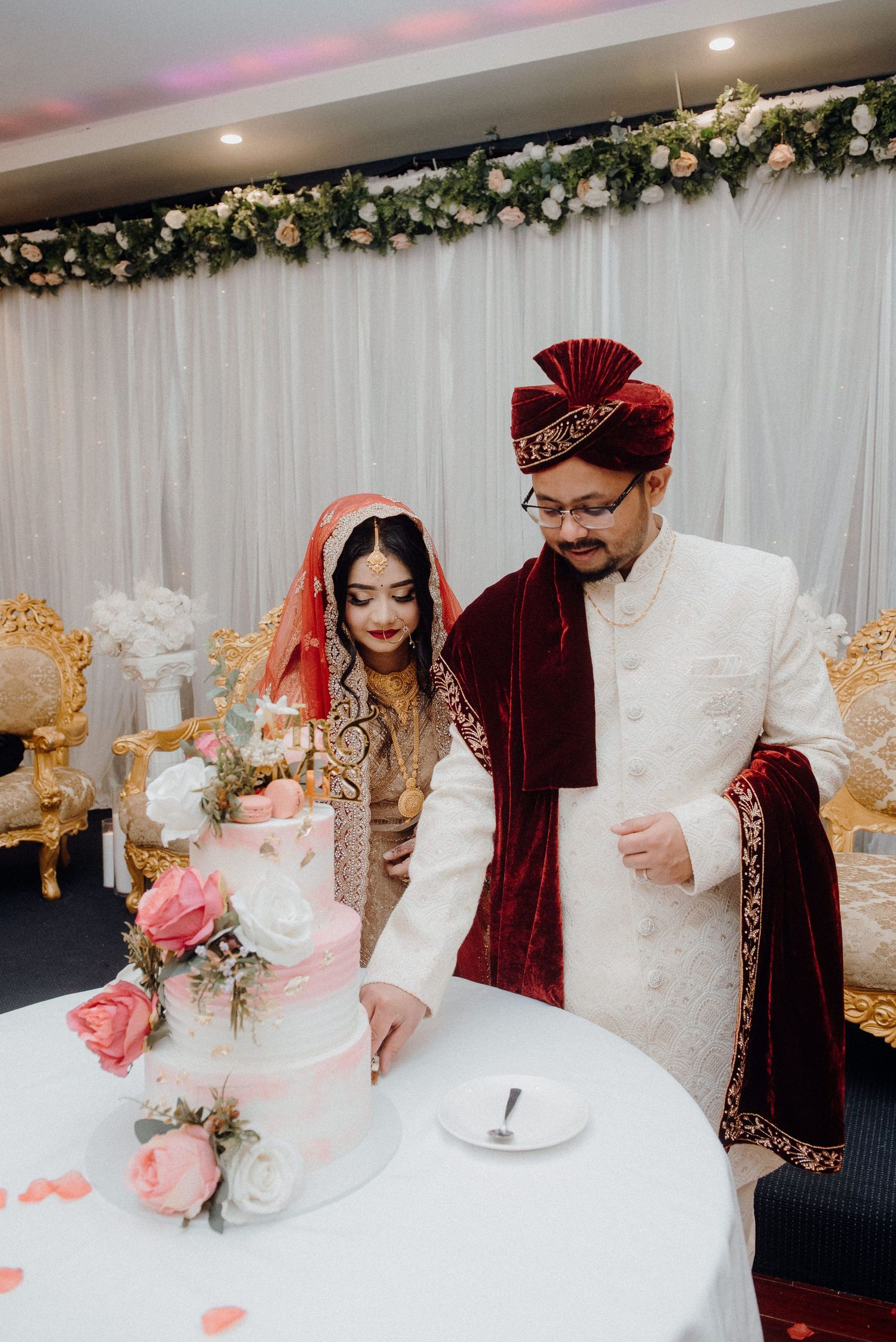 Elegant wedding cake cutting moment captured at a South Asian celebration.