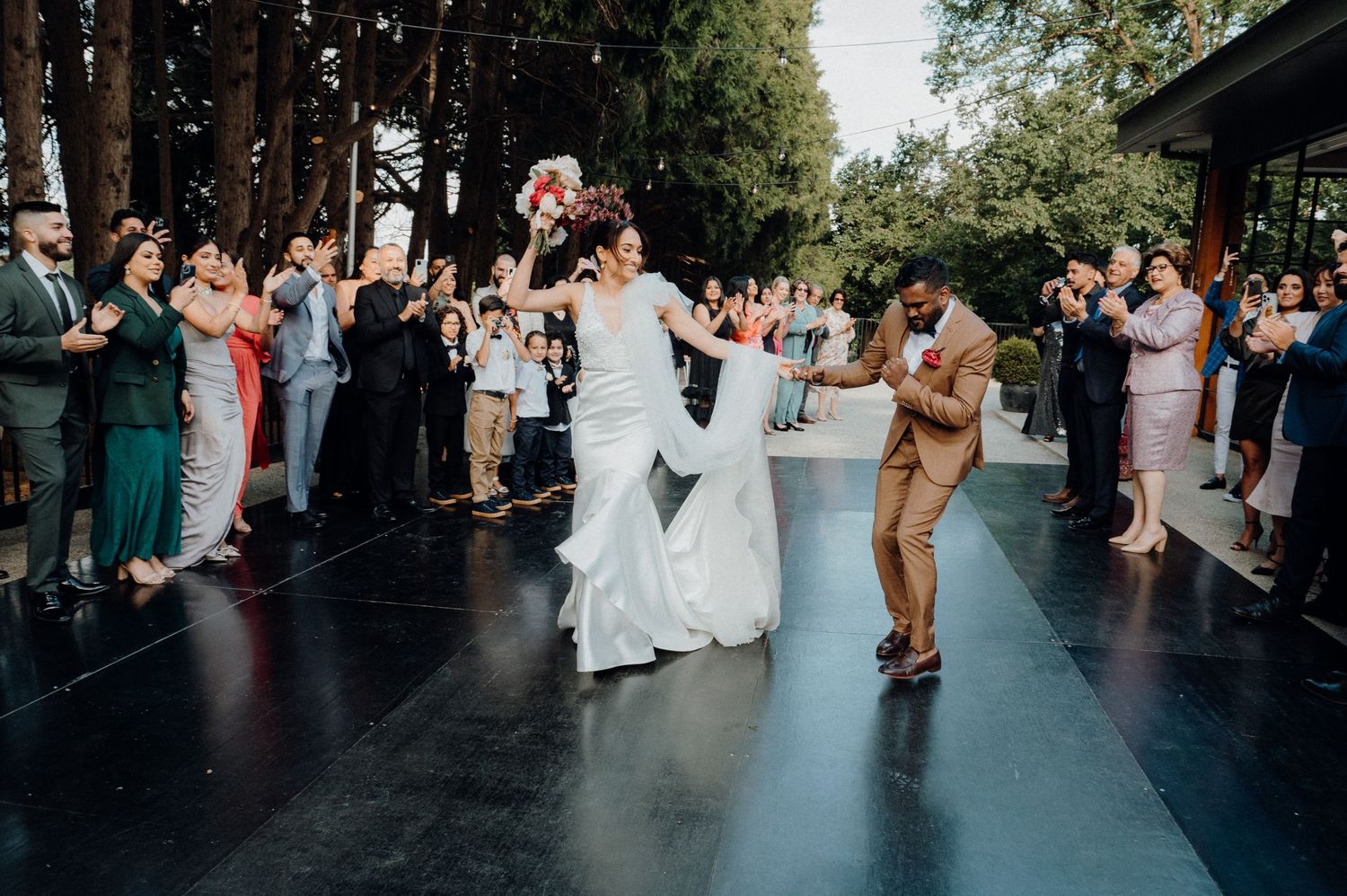 A lively first dance moment captured on an outdoor covered dance floor surrounded by wedding guests.