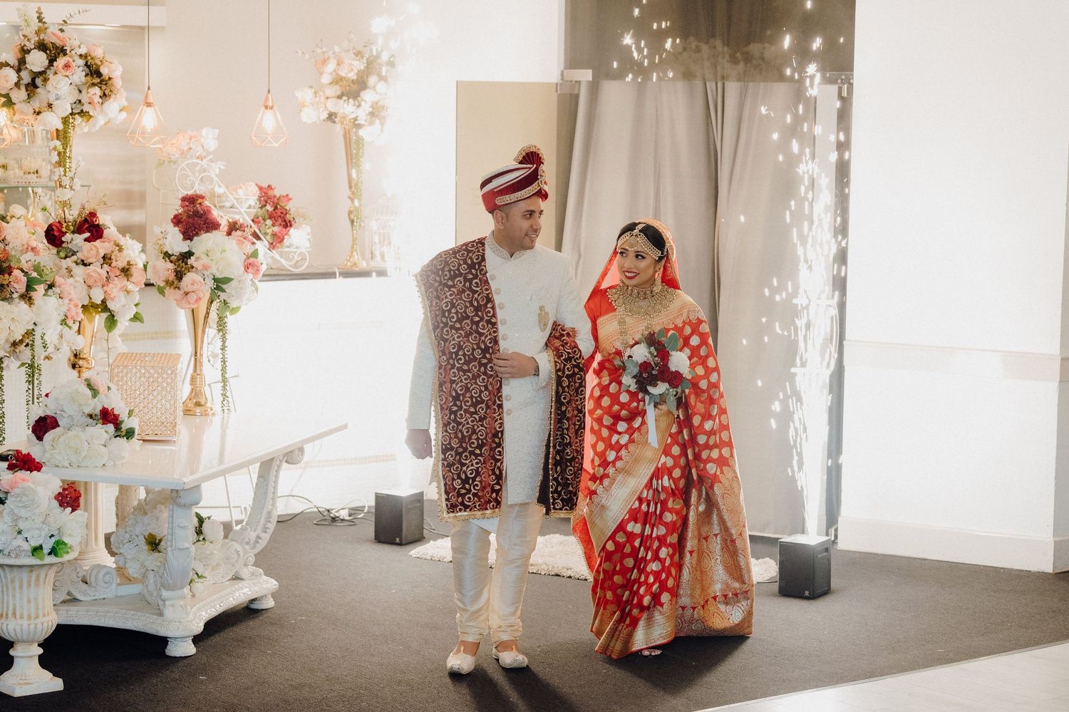Wedding couple in traditional red and white attire dancing in an elegantly decorated reception hall.