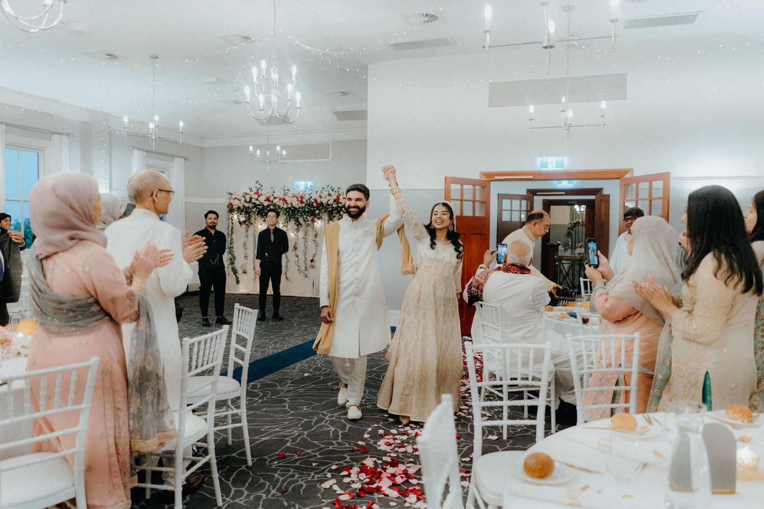 Wedding celebration with guests mingling in an elegantly decorated white reception hall.