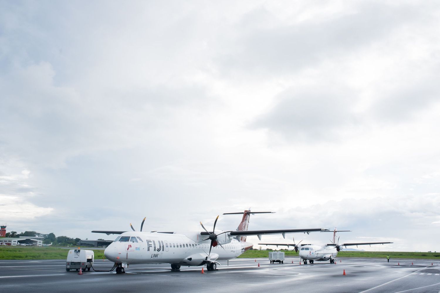 Two parked propeller aircraft on tarmac under cloudy skies.