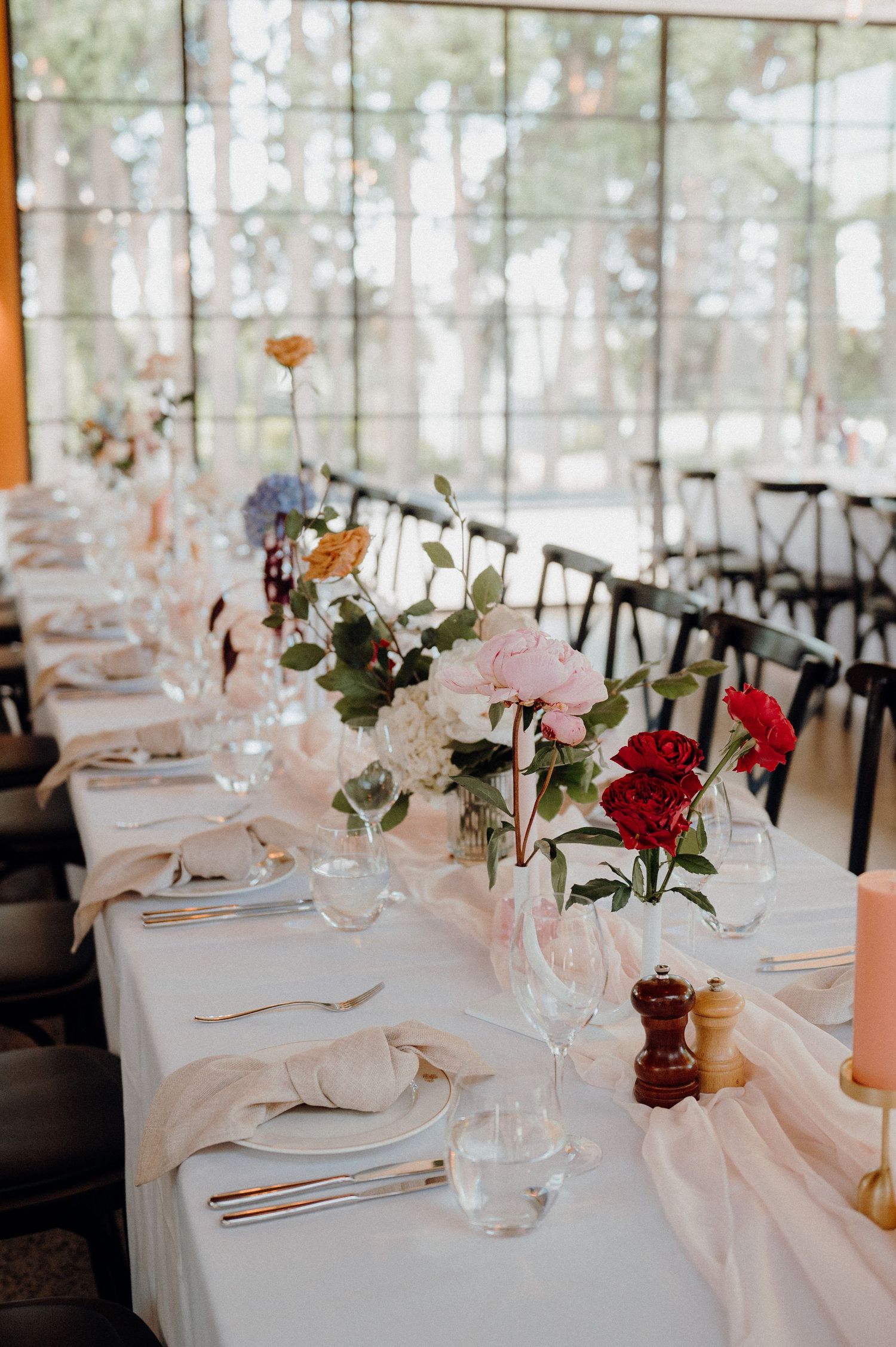 Formal table setting with colorful floral arrangements and place settings in bright venue.
